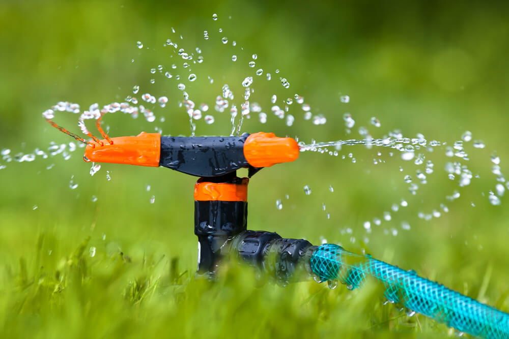 close up shot of orange and black sprinkler watering a lawn