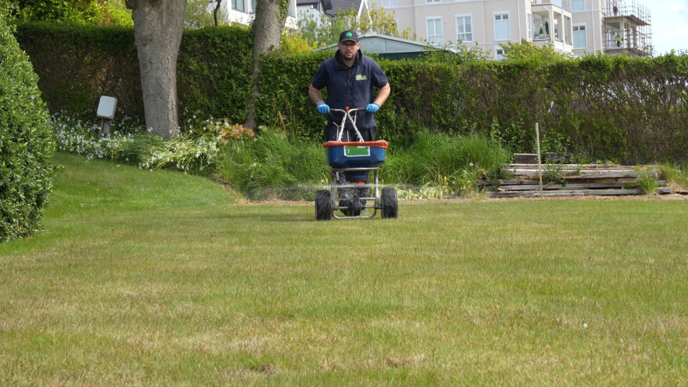 Jason from Premier Lawns pushing a branded spreader across a lawn, applying a seasonal feed