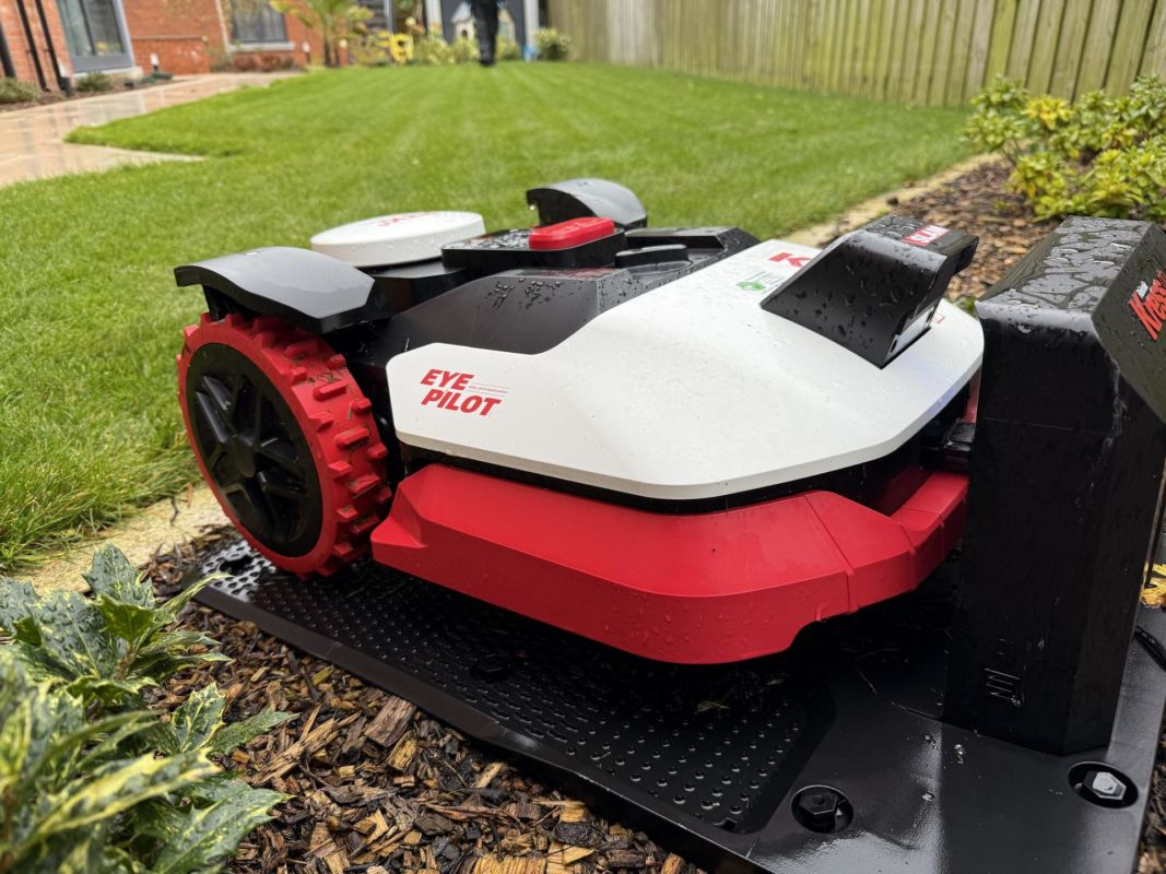Kress robot mower docked at its charging station on bark mulch, with a striped lawn behind