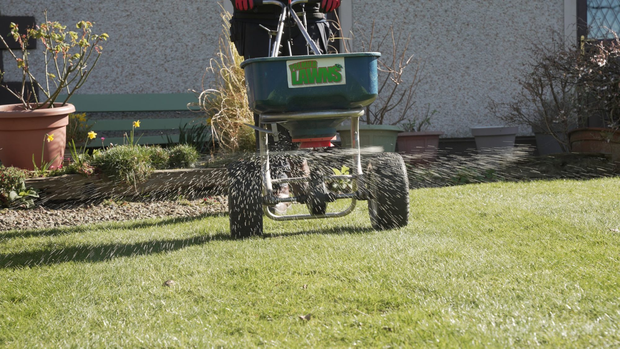 Premier Lawns spreader applying a seasonal lawn treatment in front of a house