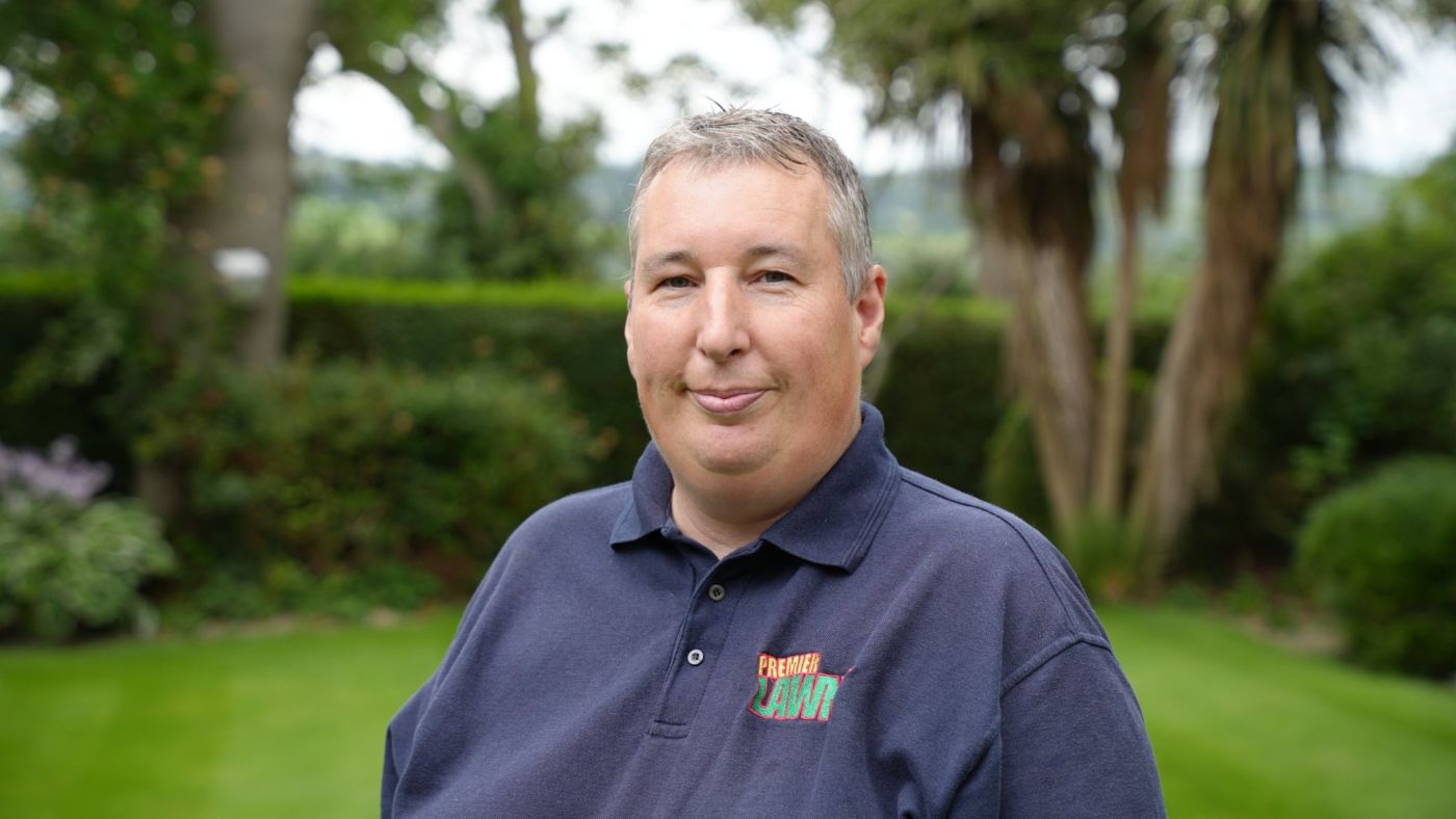 Robbie Lynn, founder of Premier Lawns, in a Premier Lawns polo shirt with a striped lawn behind him