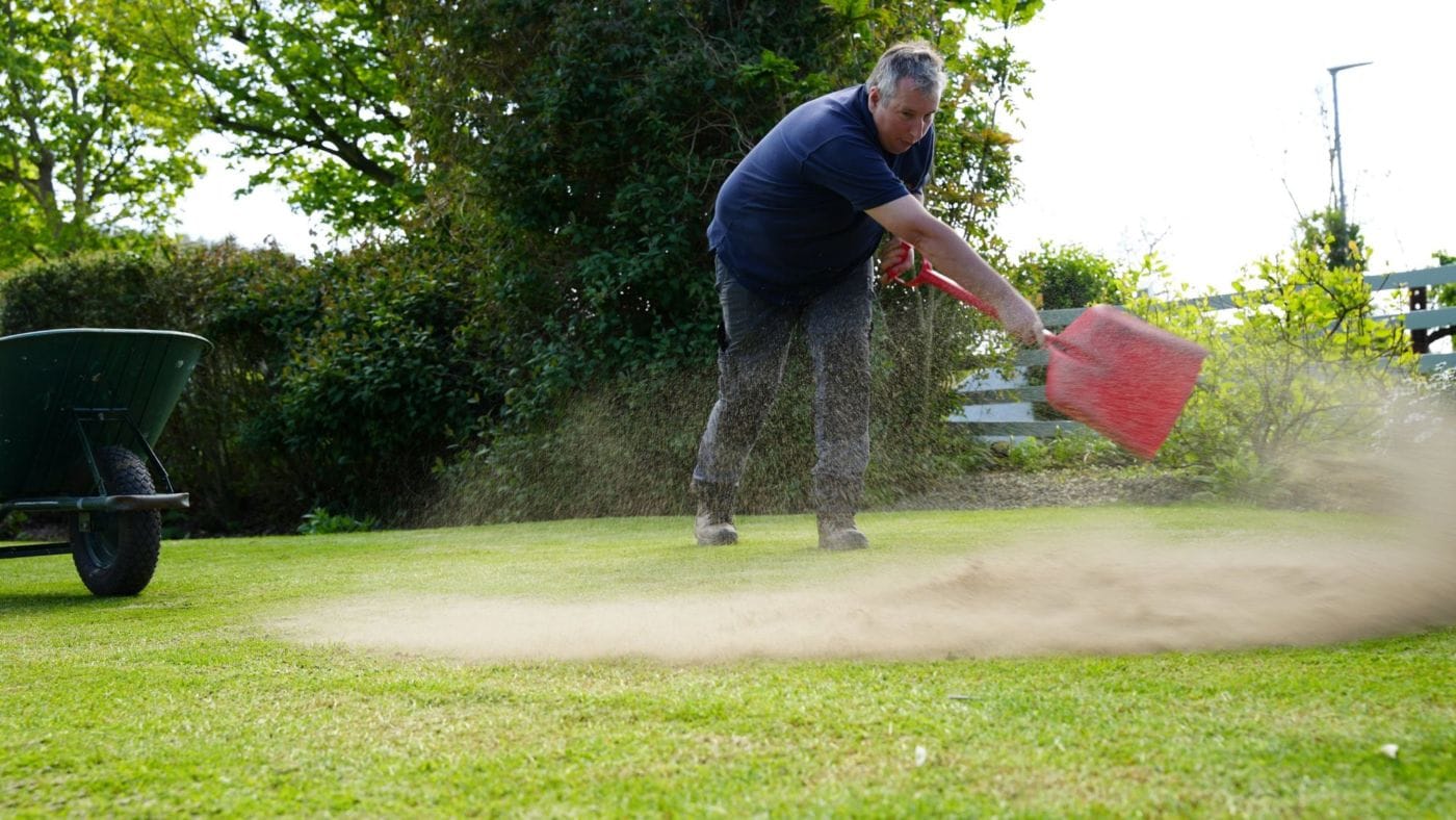 Robbie Lynn from Premier Lawns throwing topdressing across a lawn with a shovel, wheelbarrow beside him