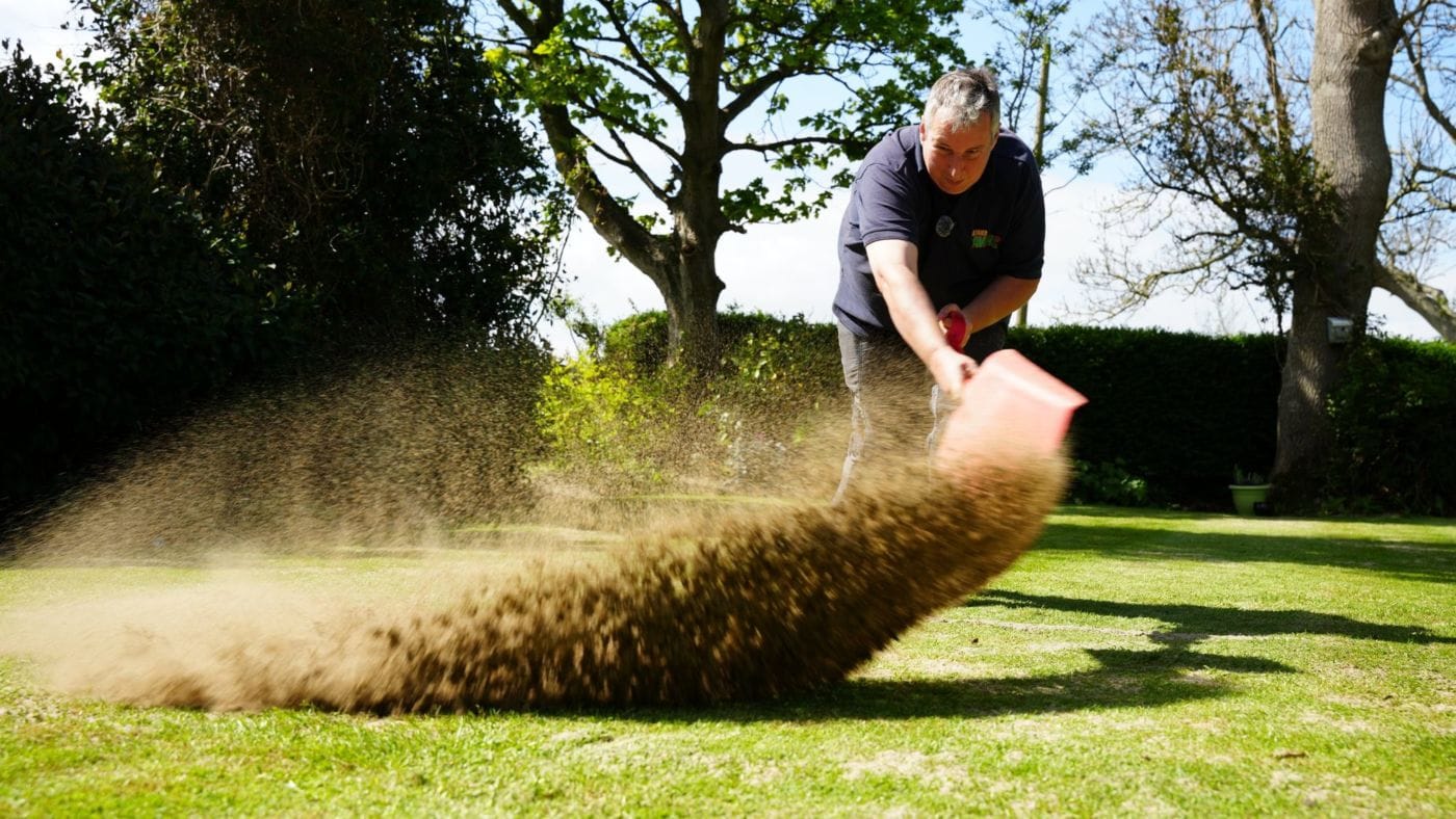 Robbie Lynn from Premier Lawns spreading a sweep of topdressing across a lawn in the sun